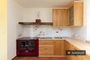 Belo kuhinjsko steklo s personaliziranim motivom rdečih rožic in vijug, vgrajeno poleg štedilnika na drva