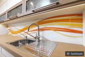 Kuhinjsko steklo: Natančna montaža kuhinjske steklene obloge za zaščito stene v kuhinji z živahnimi oranžnimi vijugami